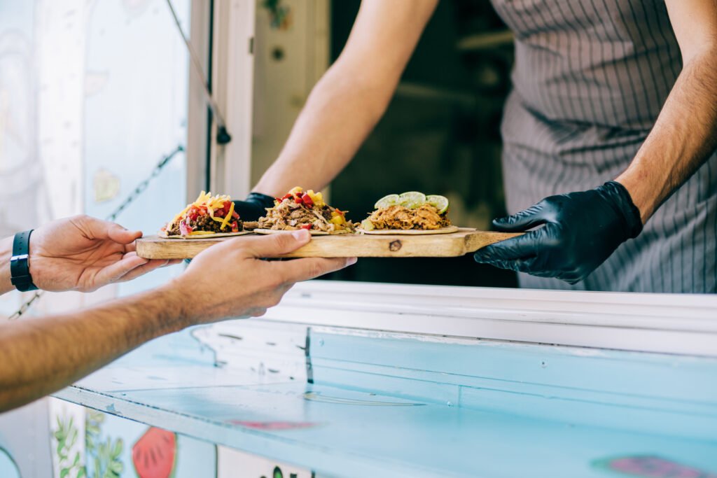 Cropped shot of young chef serving tasty tacos to male customer from the window of his food van.